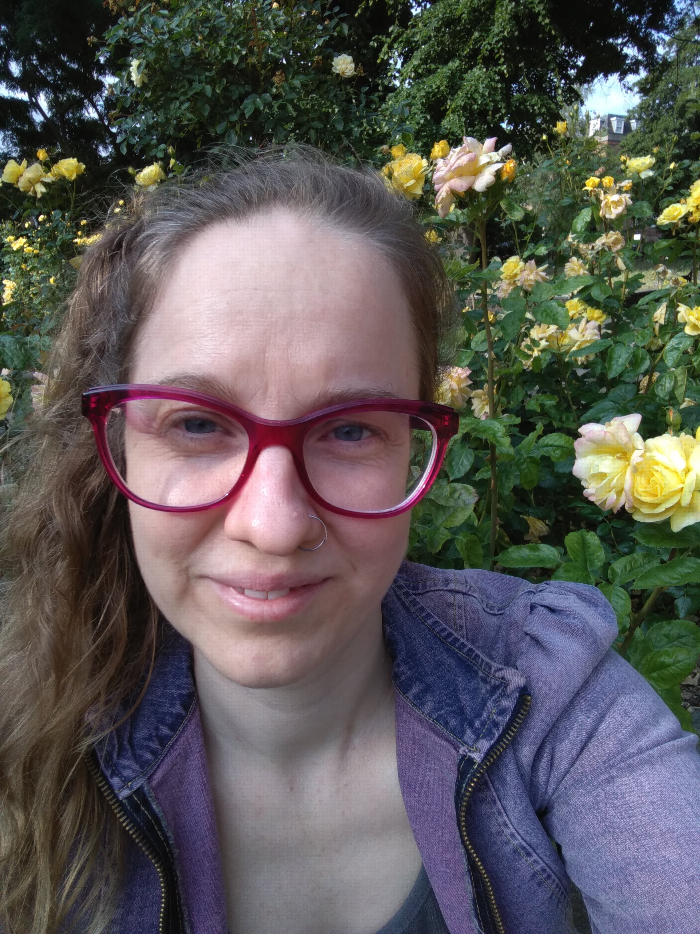 Headshot of woman with red rimmed glasses and long curly brown hair tied in ponytail.