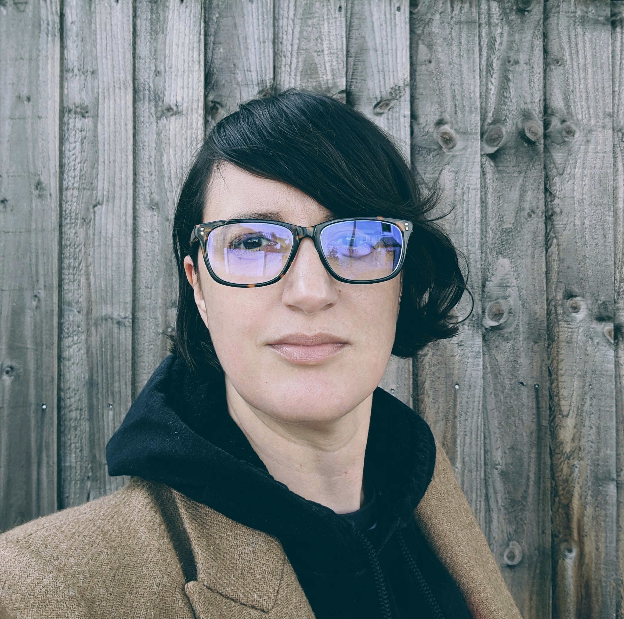 Headshot of Farah: a white woman with short dark hair, dark framed classes wearing a black hoodie and brown jacket.